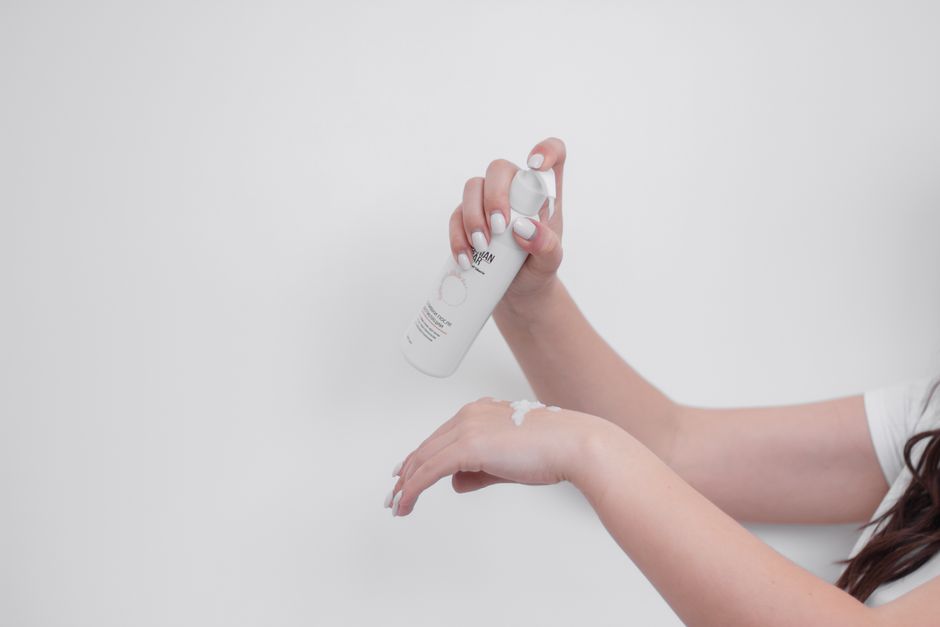 Close-up of woman's hands applying white hand cream against a white backdrop.